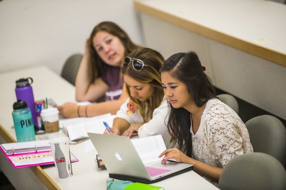 Three female students sit and take notes during class