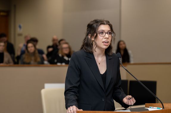 A law student stands at a podium in a courtroom.