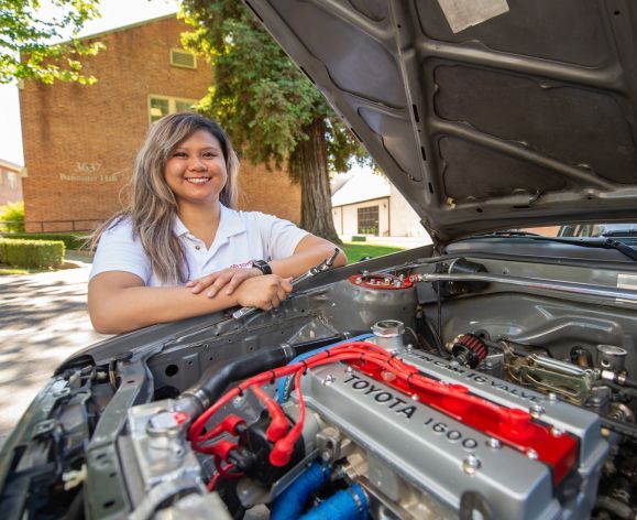 Student sitting behind engine of her custom car